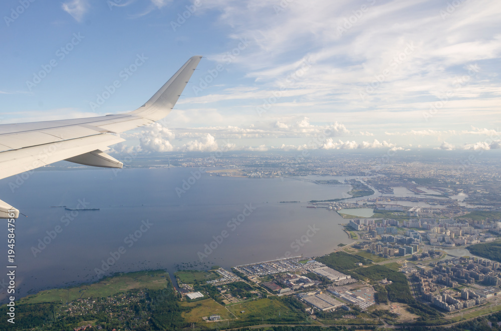 Fototapeta premium view of the aircraft wing and the city during take-off against the sky with clouds