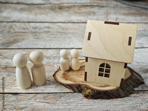 Two figures stand by a wooden house model on a wooden base as they consider options for home ownership or property investment plans for the future