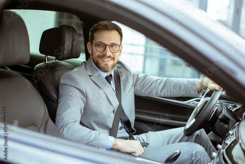 Man in suit sits in car and smiles on city street during daytime
