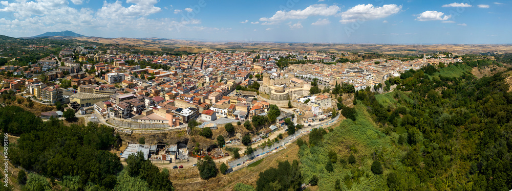 Fototapeta premium Panoramic aerial view of the city of Venosa, located in the province of Potenza, Basilicata, Italy. Italian town nestled between lush green forests. The urban center features a dense tapestry roofs.