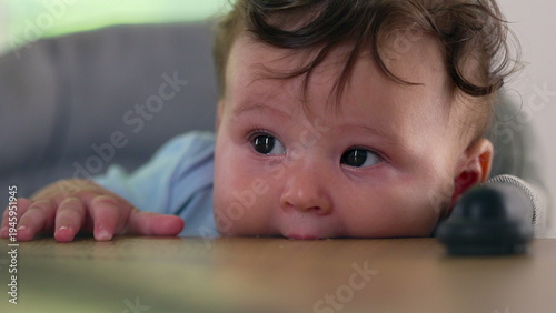 Baby lying on dining table, biting surface, big-eyed expression, early childhood sensory exploration, teething behavior, curious moment of discovery, indoor home setting
