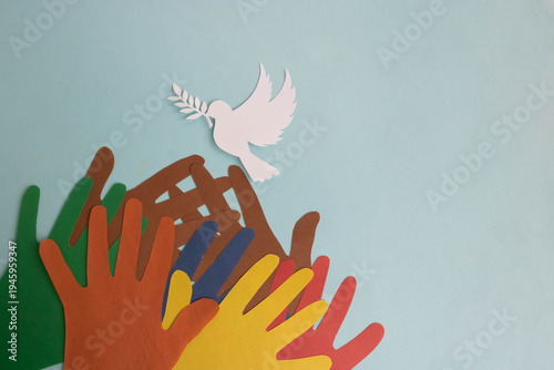 Many colorful paper hands reaching out to a paper dove of peace on a blue background. World Peace Day. Place for your text