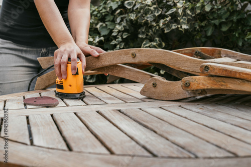 
An unrecognizable person with a homemade sander prepares their garden furniture for the arrival of warmer weather.
A woman with a sander on her small terrace. People, lifestyles.