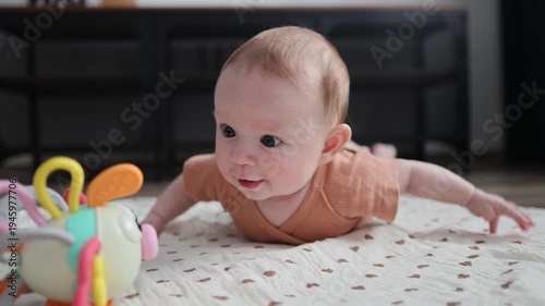 Infant lying on a mat, lifting chest and arms while looking at a toy and the camera