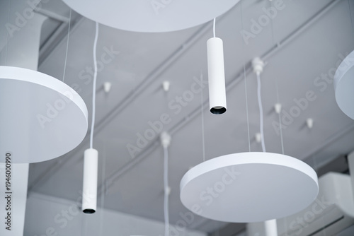 Minimalist hanging ceiling lights with circular and cylindrical fixtures in a trendy interior. Stylish architectural illumination for modern workspace or gallery design. Photo