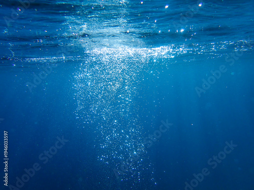 Ocean blue underwater with sunrays, Underwater Sea Deep Water Abstract Sunshine, sea wave , clean waters in summer time, Natural underwater seascape, sand on ocean floor and water surface sunlight.