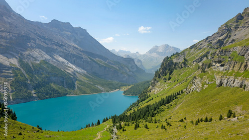 Bild auf Leinwand Oeschinen Lake in the Swiss Alps with turquoise water, green slopes, and rocky mountains under a clear summer sky