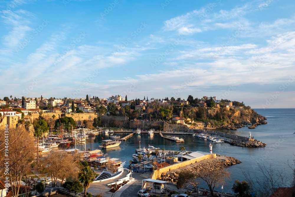 Obraz premium Panoramic view of Kaleici marina and the historic old town of Antalya with boats in the harbor and warm golden hour sunset light illuminating the Mediterranean coastline in southern Türkiye.