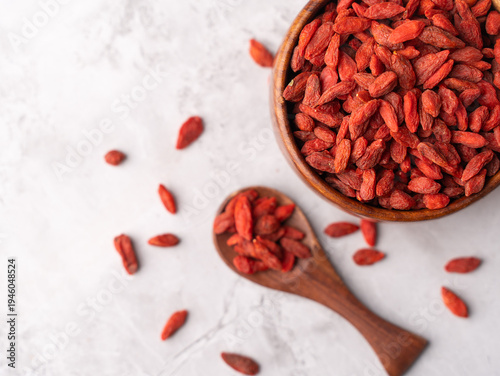 Cuadro en lienzo Dried Goji berries or Wolfberry scattered, vibrant red, in a wooden bowl on a textured background