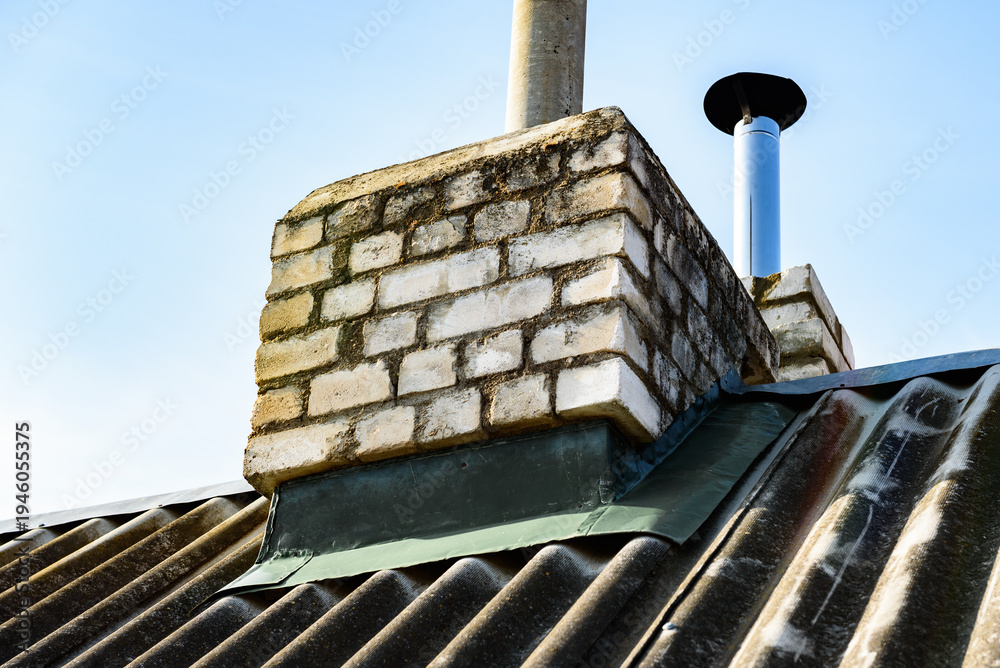 Fototapeta premium Chimney pipe from stainless steel on the roof of the house. Repair of roof chimney, brickwork.