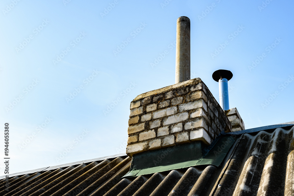 Fototapeta premium Chimney pipe from stainless steel on the roof of the house. Repair of roof chimney, brickwork.