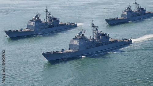 Group of modern naval warships sailing together in formation across open ocean waters. Concept of military power, maritime defense, and security patrol. Identifiable markings on ships removed. 