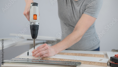 A Caucasian woman uses a screwdriver to tighten a screw while assembling a cabinet.