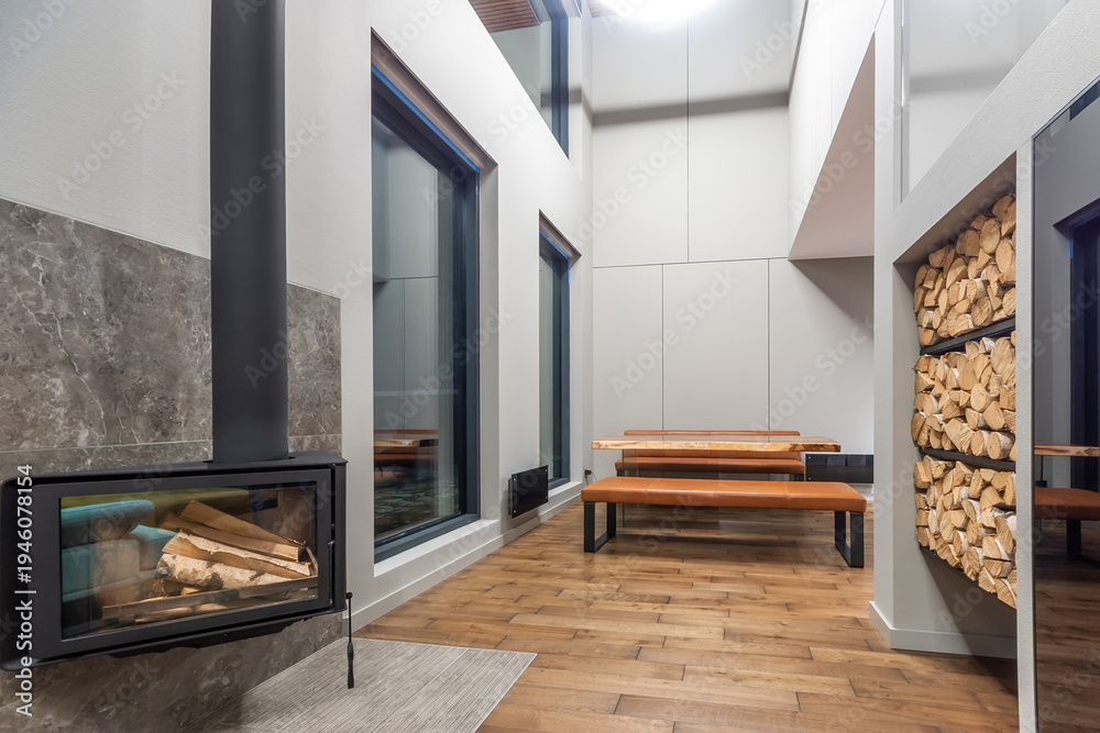 Fototapeta premium The interior of a country house in high-tech style. White decor with elements of black. A modern oven with a glass heat-resistant door. A place to store firewood.