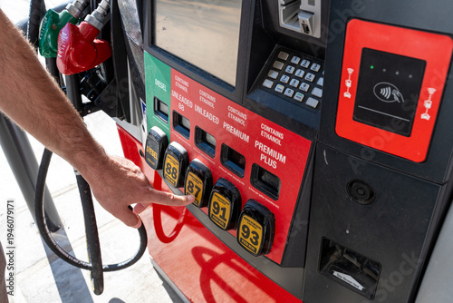 Male hand choosing 87-octane gasoline at a US gas station and showing the high price of gas