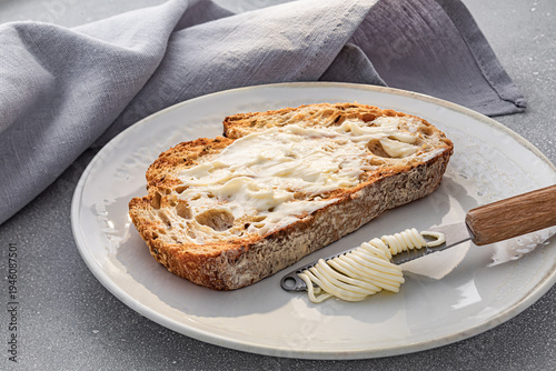 Crispy toasted artisan bread with a fresh butter curl on a knife. Close-up of morning breakfast on a plate with soft lighting. Natural organic dairy product and bakery texture.