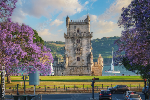 View of Belem Tower surrounded by beautiful purple jacaranda flowers on the Tagus River during sunset in Lisbon. Belem, Lisbon, Portugal