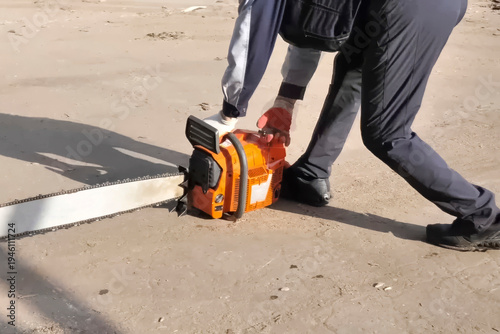 The worker, leaning on the ground, starts the chainsaw.