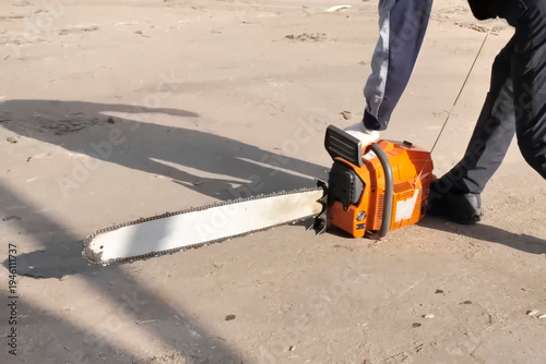 The worker, leaning on the ground, starts the chainsaw.