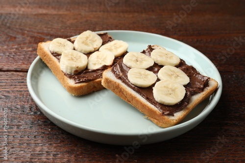 Toasts with chocolate paste and banana on wooden table, closeup