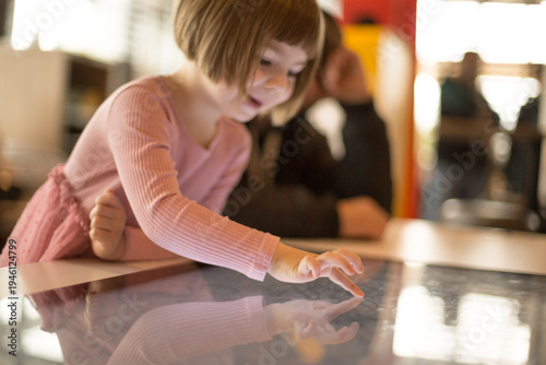 Girl uses touchscreen device for educational purposes, engaging with digital learning materials. Modern technology supports early childhood development through interactive and intuitive tools.