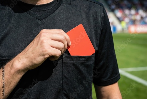 Soccer referee reaching into his shirt pocket to pull out a red card during a match