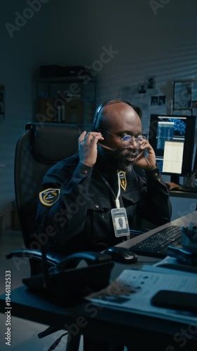 Vertical shot of African American man as police officer picking up phone and making calls in control room during night shift