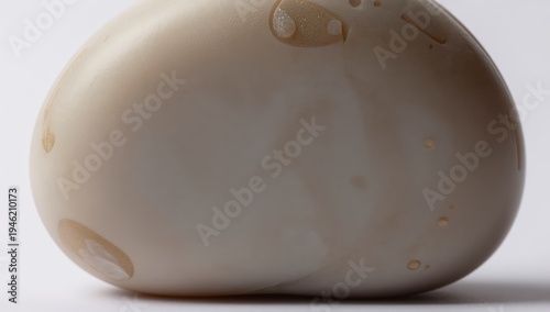 Close up of a smooth pale beige round object with subtle light brown textured patterns and small liquid droplets