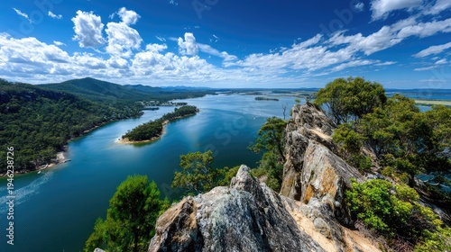 Breathtaking Aerial View of a Serene River Valley Surrounded by Lush Green Forests and Dramatic Clouds Under a Bright Blue Sky
