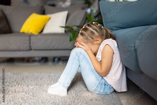 Photos Upset young girl sitting on floor covering her face in living room