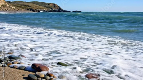 Wallpaper Mural Waves Crashing on Pebble Beach with Clear Blue Skies and Rolling Green Coastal Mountains in Background Torontodigital.ca