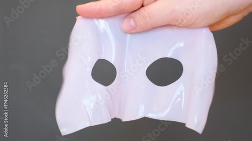 A woman's hand holds a gel sheet mask on gray background close-up.