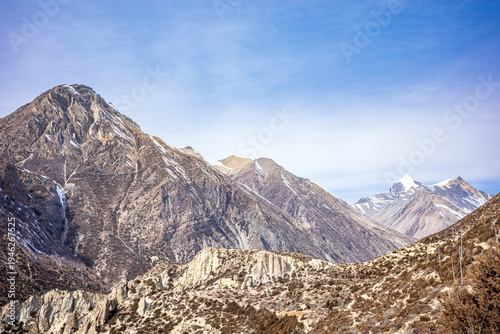 Wide panoramic view of rugged Himalayan mountain peaks and dry alpine hills in the Annapurna region of Nepal. The dramatic landscape features layered rocky ridges, distant snow-capped summits