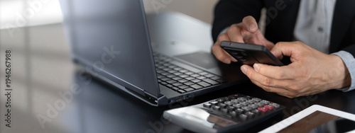 Businessman using smartphone with laptop and calculator for mobile finance and budgeting