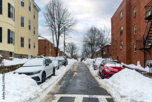 Obraz na płótnie Snow-covered residential street with parked cars and brick buildings in Brighton