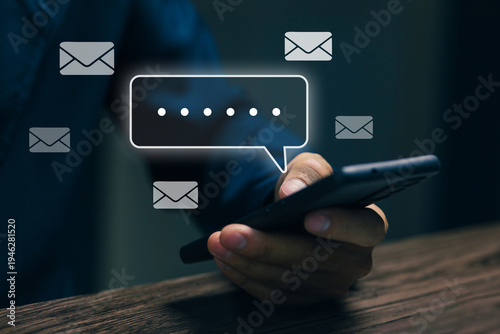 Businessman holding smartphone with digital messaging interface and email icons. Concept of mobile communication, online chat, instant messaging, digital conversation and modern business connectivity.