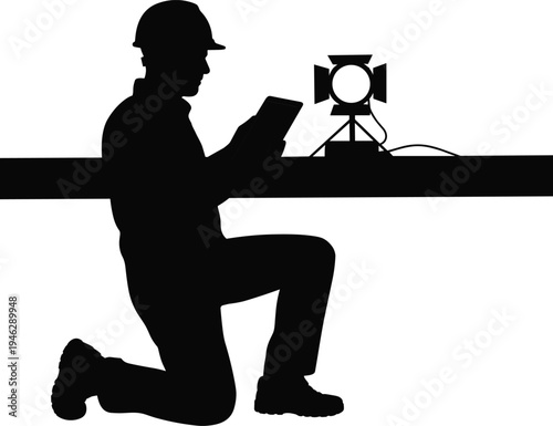 Silhouette videographer kneeling with tablet beside studio spotlight on desk, professional filmmaker lighting setup, video production workspace concept, vector illustration