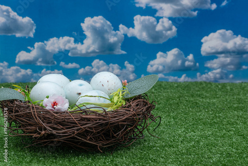 Light blue speckled Easter eggs in a nest on green grass.