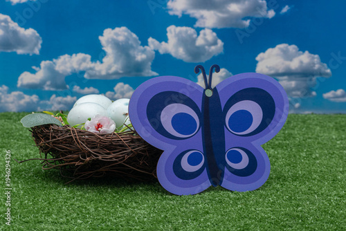 Large purple butterfly decoration and bird's nest with blue eggs on green grass.