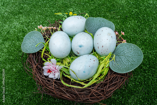 Top view of a bird's nest with light blue speckled eggs on green grass.