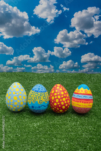 Row of four hand-painted colorful Easter eggs on green grass under a blue sky.