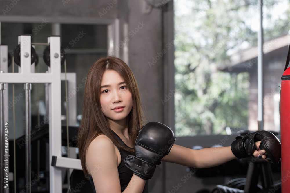 Fototapeta premium Asian female boxer wearing boxing gloves while training with punching bag in gym, demonstrating focus and strength during combat sport workout session.