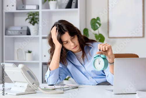 Cuadro en lienzo Stressed young businesswoman with alarm clock at her workspace in office