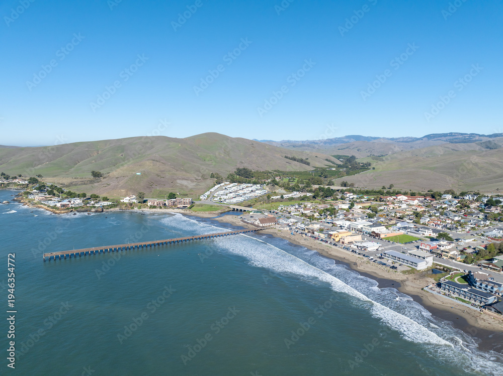 Fototapeta premium Aerial view of Cayucos, California USA, Pier and Ocean Ave and Shoreline Beach with Green Hills and Central Coast in San Luis Obispo County. High quality 4k footage