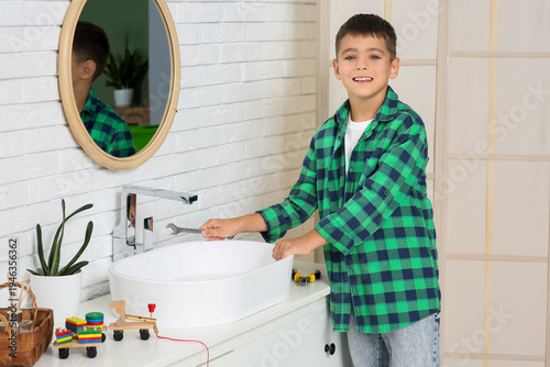 Cute little happy plumber with wrench repairing sink in bathroom