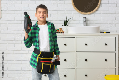 Cute little happy builder with electric drill working in bathroom