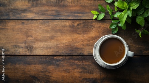 Overhead view of a cup of tea on wooden table with green leaves