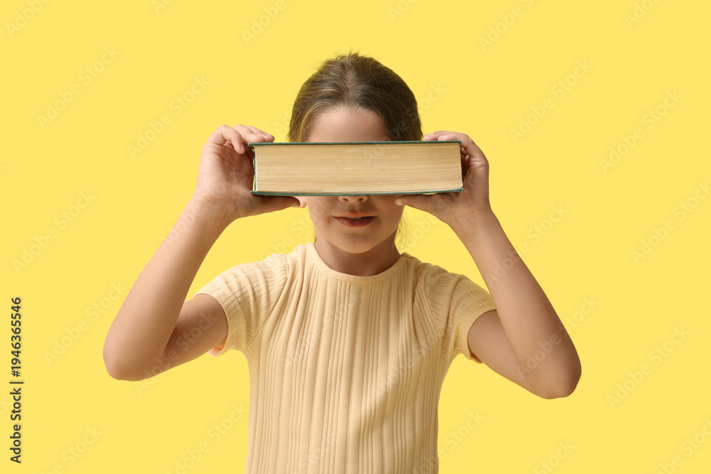 Naklejka premium Cute little girl holding book on yellow background
