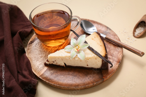 Wooden plate with piece of sweet vanilla cheesecake and glass cup of tea on yellow background