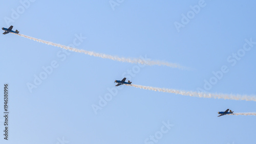 Three aerobatic aircraft performing a synchronized aerial maneuver with curved smoke trails against a clear blue sky during an aviation airshow. Dynamic formation display in an open sky background